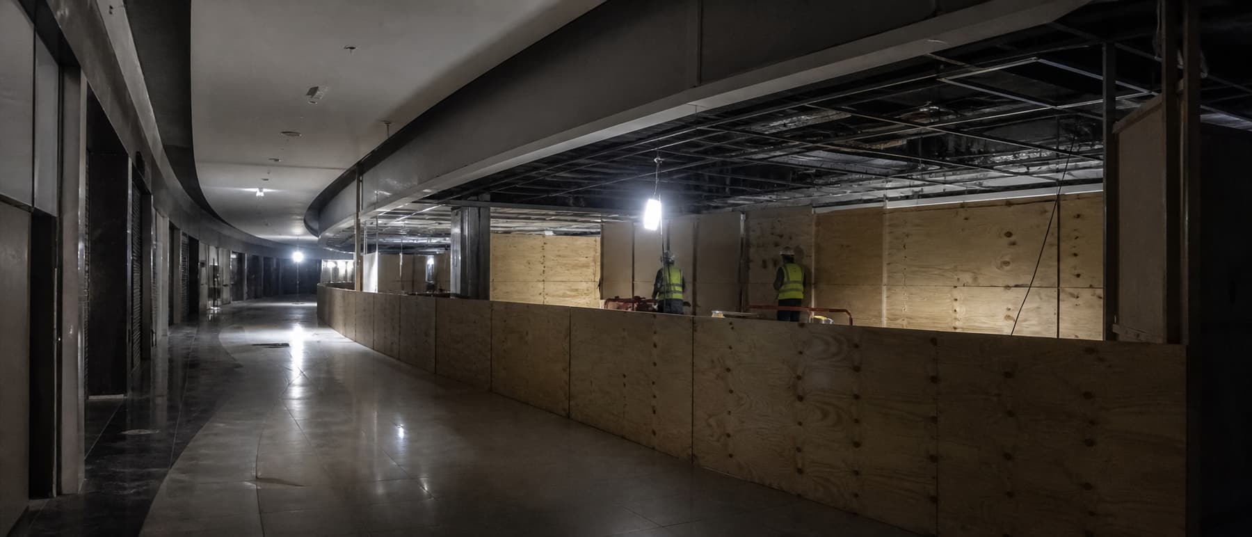 A crew working under work lights on a shopping mall trading floor after closing, with hoarding in place.